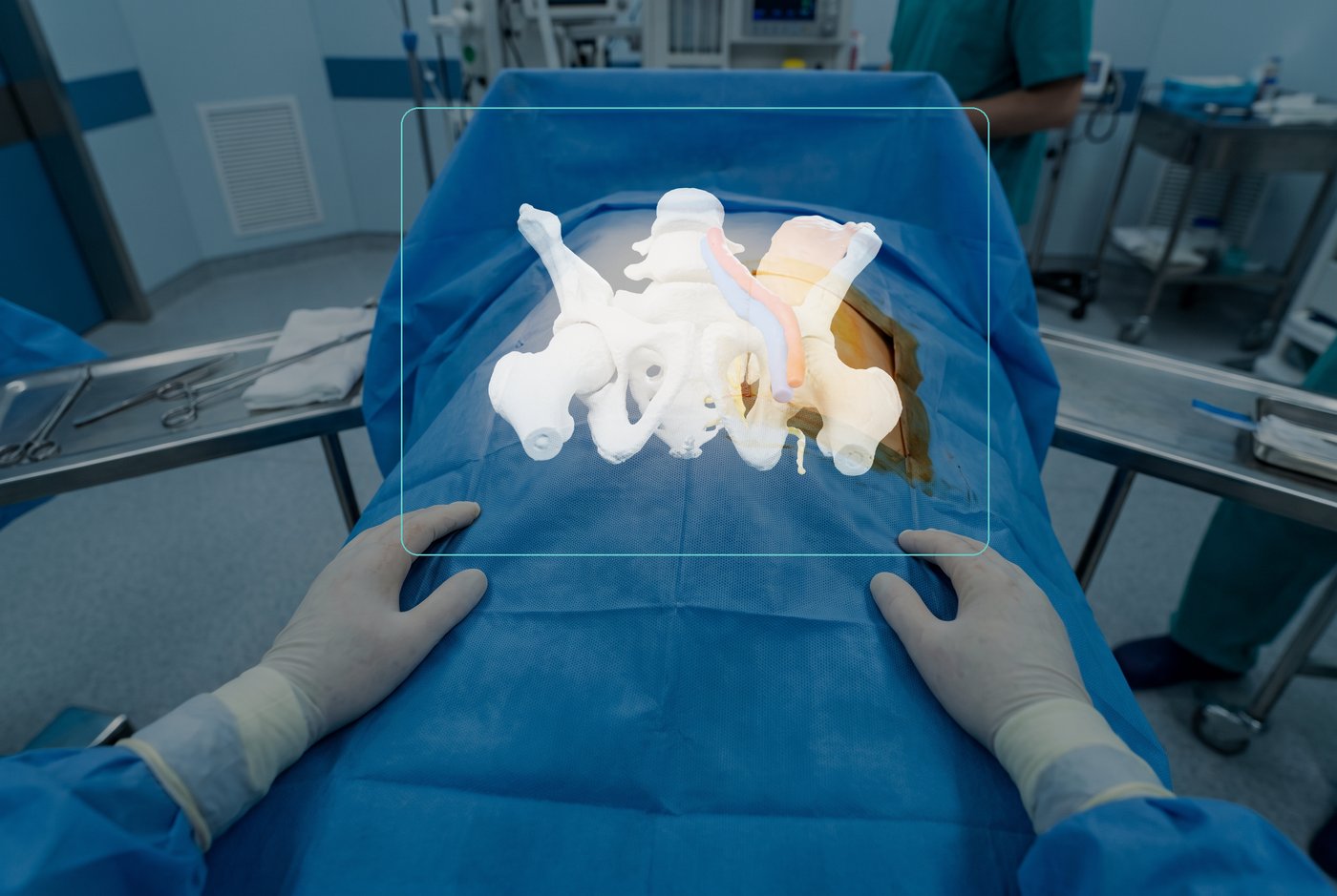 A surgeon’s view through a see-through headset of a draped patient: the pelvis model is drawn as light over the patient's draped lower body, inside a rectangle.